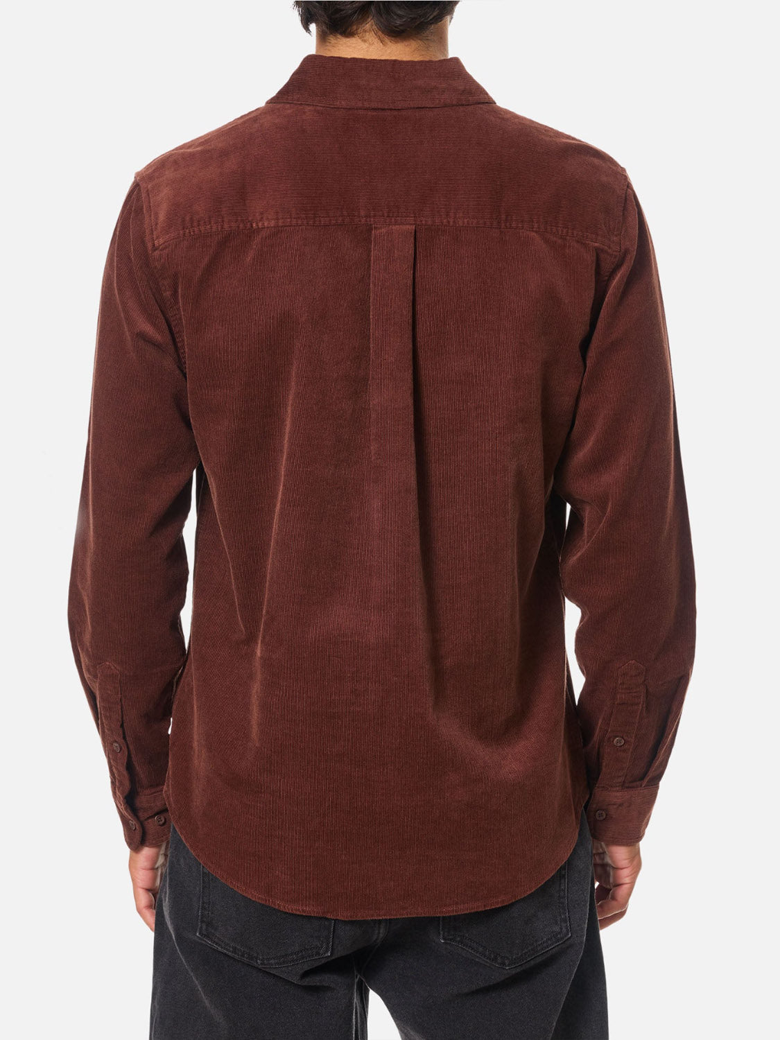 A person stands facing away, showcasing the back of the Katin Granada Shirt—a long-sleeve, dark brown cotton corduroy button-down—paired with black pants against a white background.