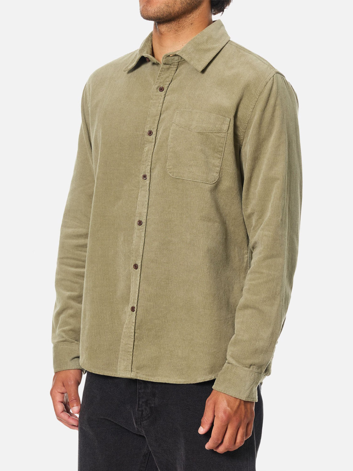 A person in an olive green Katin Granada Shirt, a men's corduroy shirt with a chest pocket, and black pants stands against a white background.