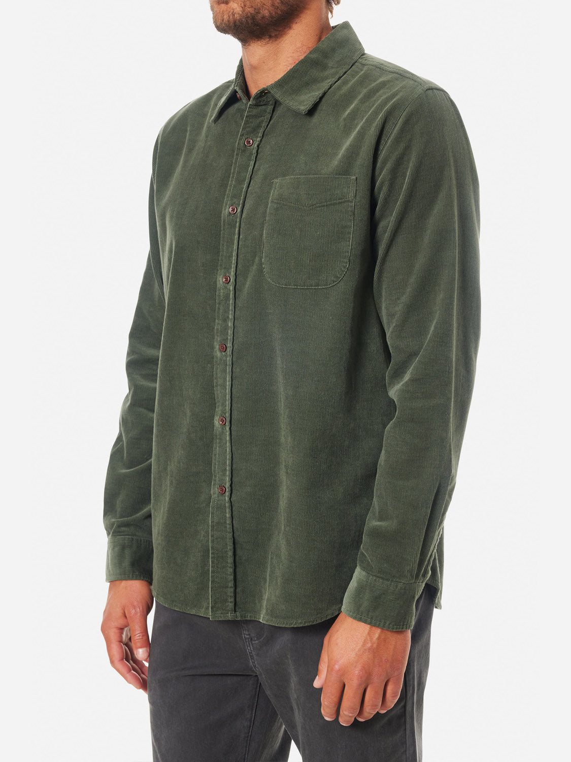 A person in a green Katin Granada Shirt made of cotton corduroy with a chest pocket pairs it with black pants, standing side-on against a plain white backdrop.