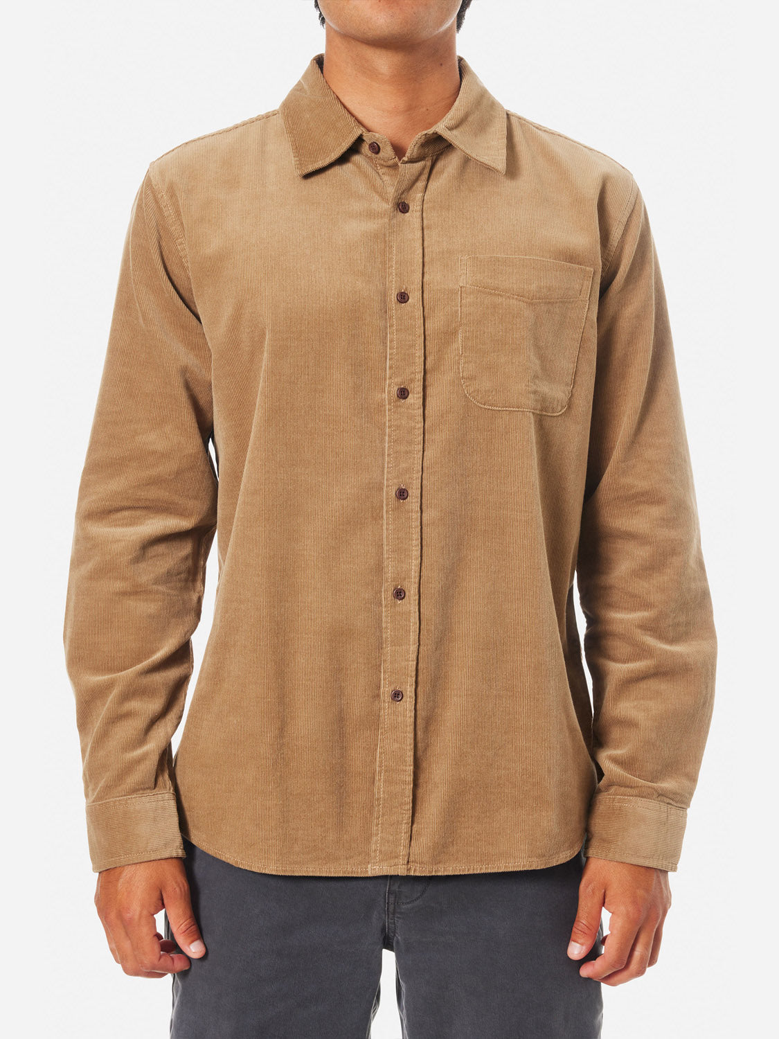 A person models the Katin Granada Shirt from the fall collection—a beige corduroy button-up with a chest pocket, long sleeves, and small buttons. Its paired with dark pants against a plain white background.