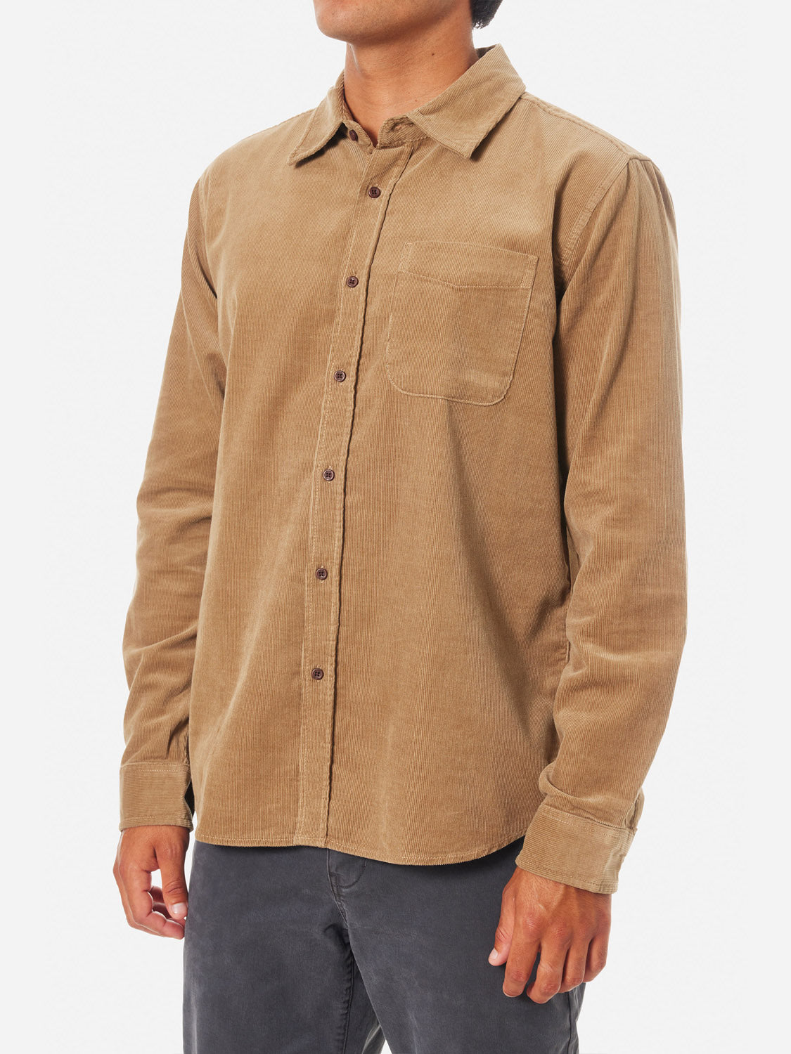 Wearing Katins Granada Shirt from the fall collection, made of cotton corduroy in light brown with a front pocket and dark buttons, the person pairs it with dark pants against a white backdrop, accentuating the ensembles timeless appeal.
