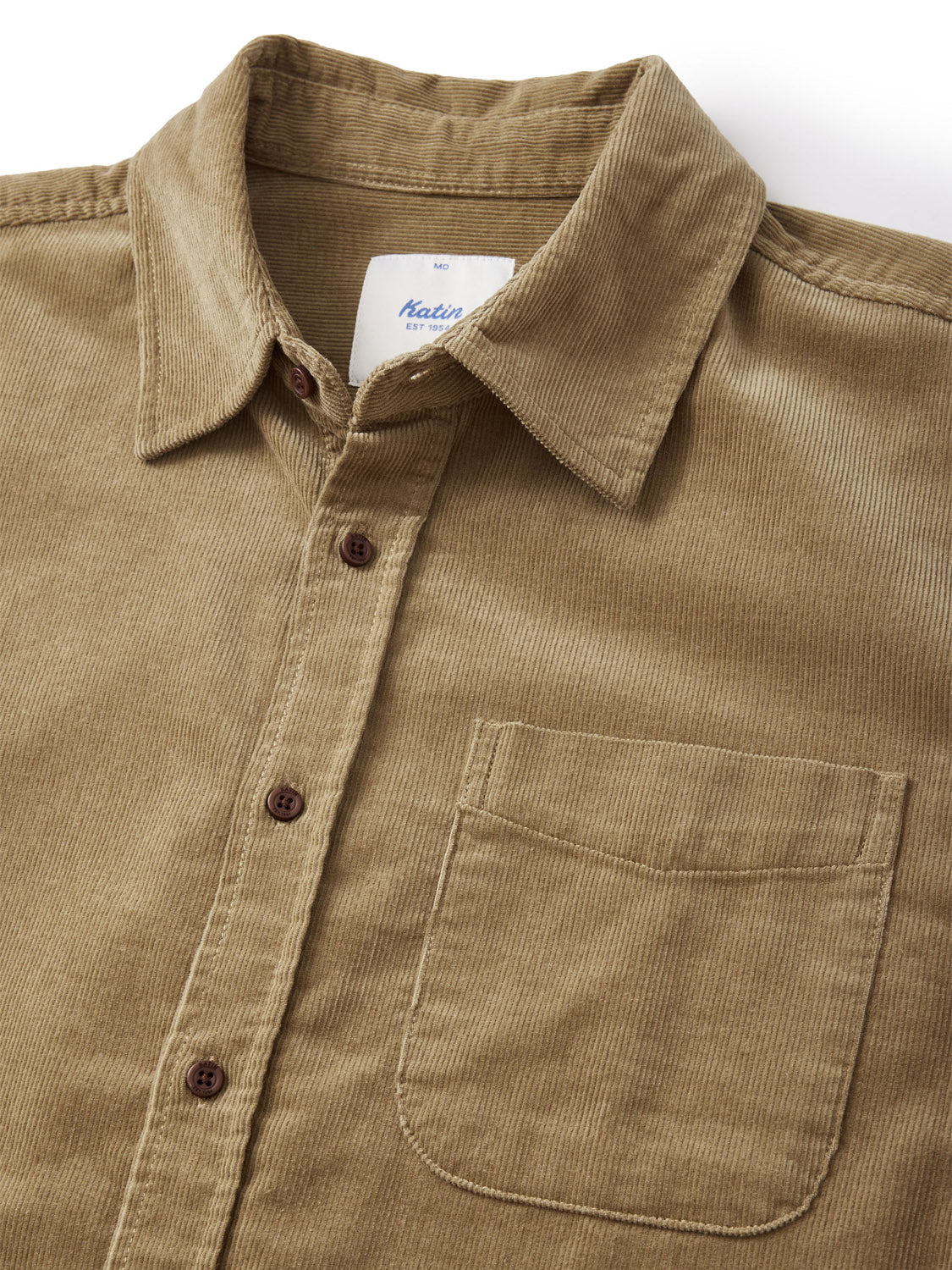 The Katin Granada Shirt from our fall collection is a tan cotton corduroy button-up featuring a pointed collar, brown buttons, and a chest pocket. A white label with blue text is visible inside the collar. The fabric has a textured, slightly ribbed look.