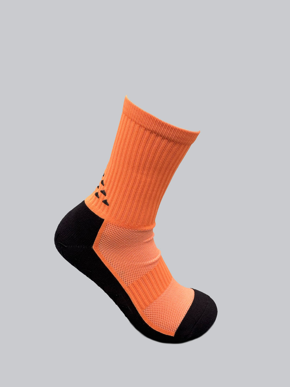 Displayed against a grey background, the ID Menswear Grip Sports Socks feature an anti-slip design for enhanced performance and comfort, highlighted by their vibrant orange color with black accents on the heel and toe, plus a subtle black geometric pattern on the side.