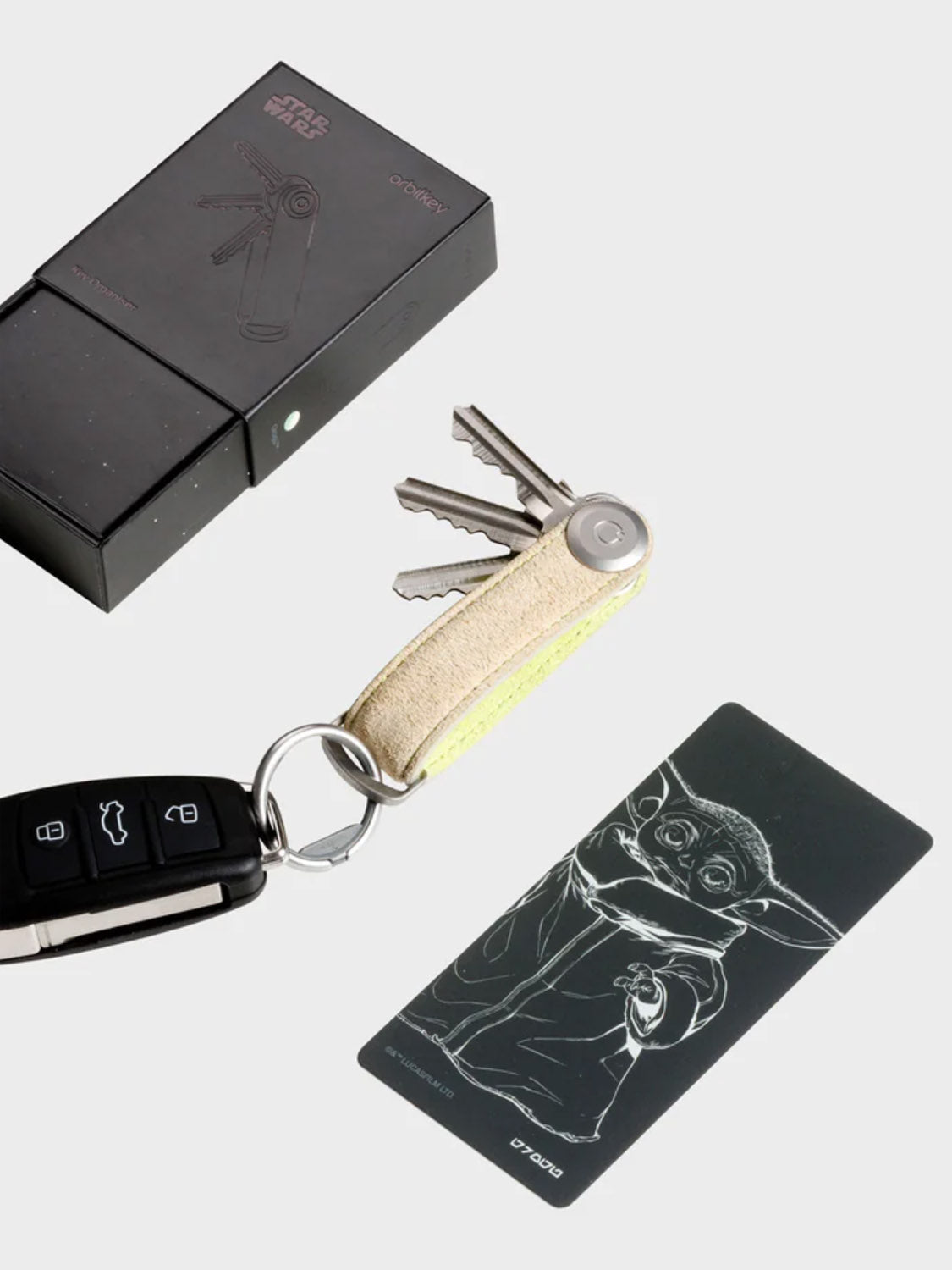 An Orbitkeys Star Wars Grogu Key Organizer and a car fob sit beside a black box and a card displaying Grogu (Baby Yoda) from Star Wars.