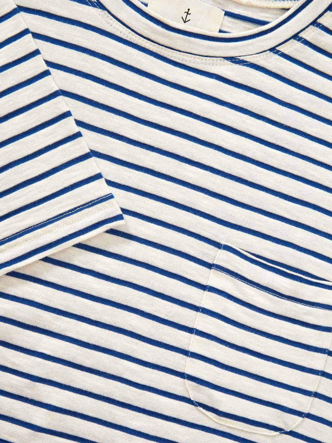Close-up of the La Paz Guerreiro Tee, a soft fabric white t-shirt with horizontal blue stripes, chest pocket, and an anchor tag. This lightweight cotton design from La Paz combines comfort and style, making it perfect for summer.