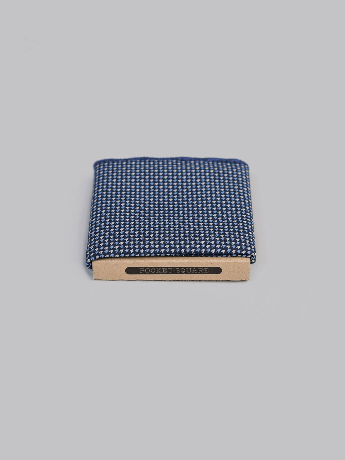 ID Menswear’s Hana Ya Pocket Square, featuring a folded navy blue and white Japanese print, is displayed in a cardboard holder labeled “Pocket Square” against a plain light gray background.