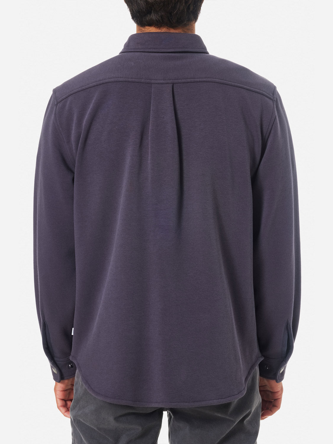 A person is seen from behind, wearing a Katin Harold Fleece Jacket with a collar and snap closures in dark blue. It features a central back pleat and buttoned cuffs. Theyre paired elegantly with gray pants, creating a sophisticated ensemble.