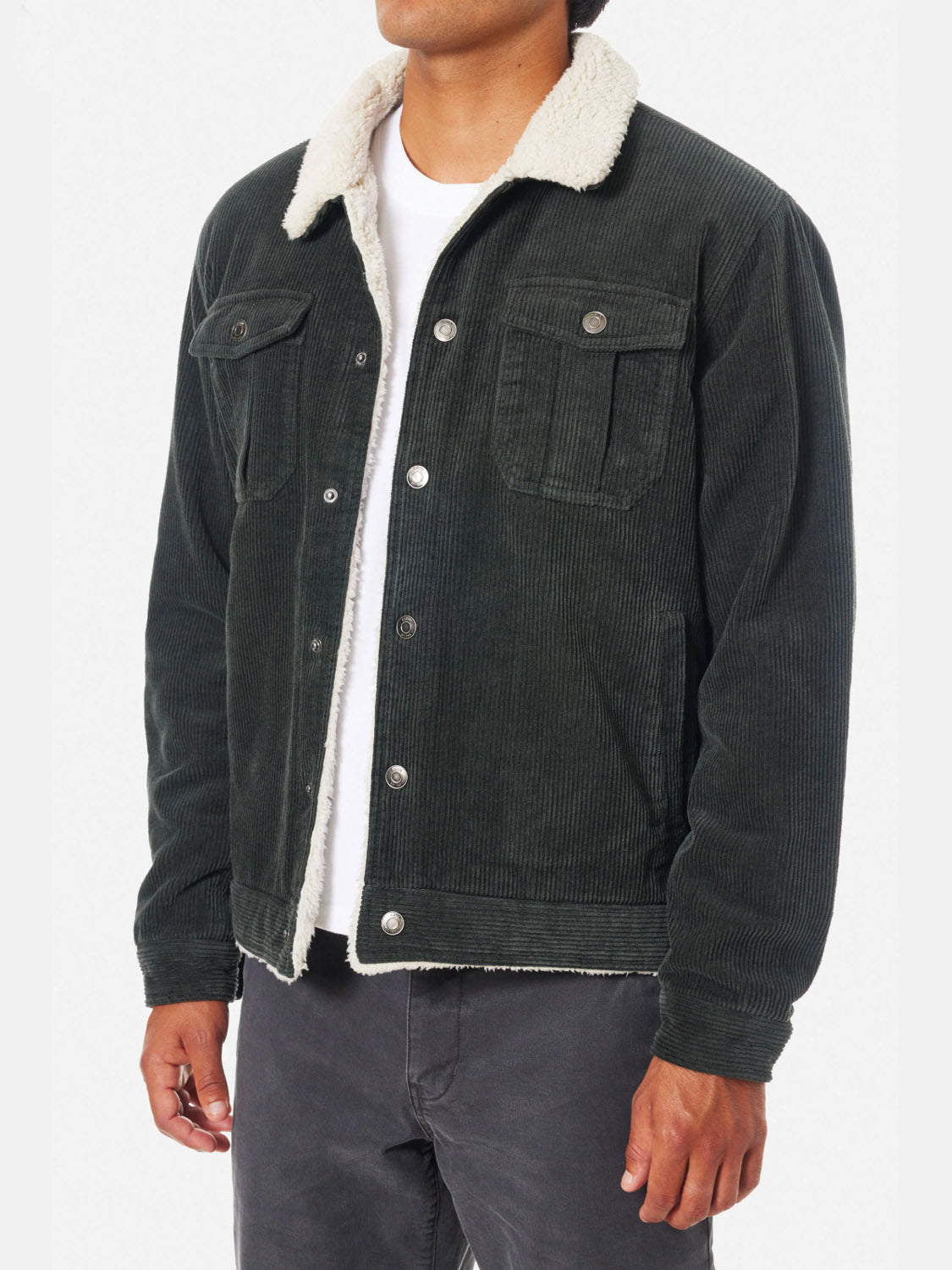 A person wears the Katin Harris Corduroy Jacket—a dark green sherpa-lined piece with a white collar—over a white T-shirt and dark pants, standing against a plain light background.