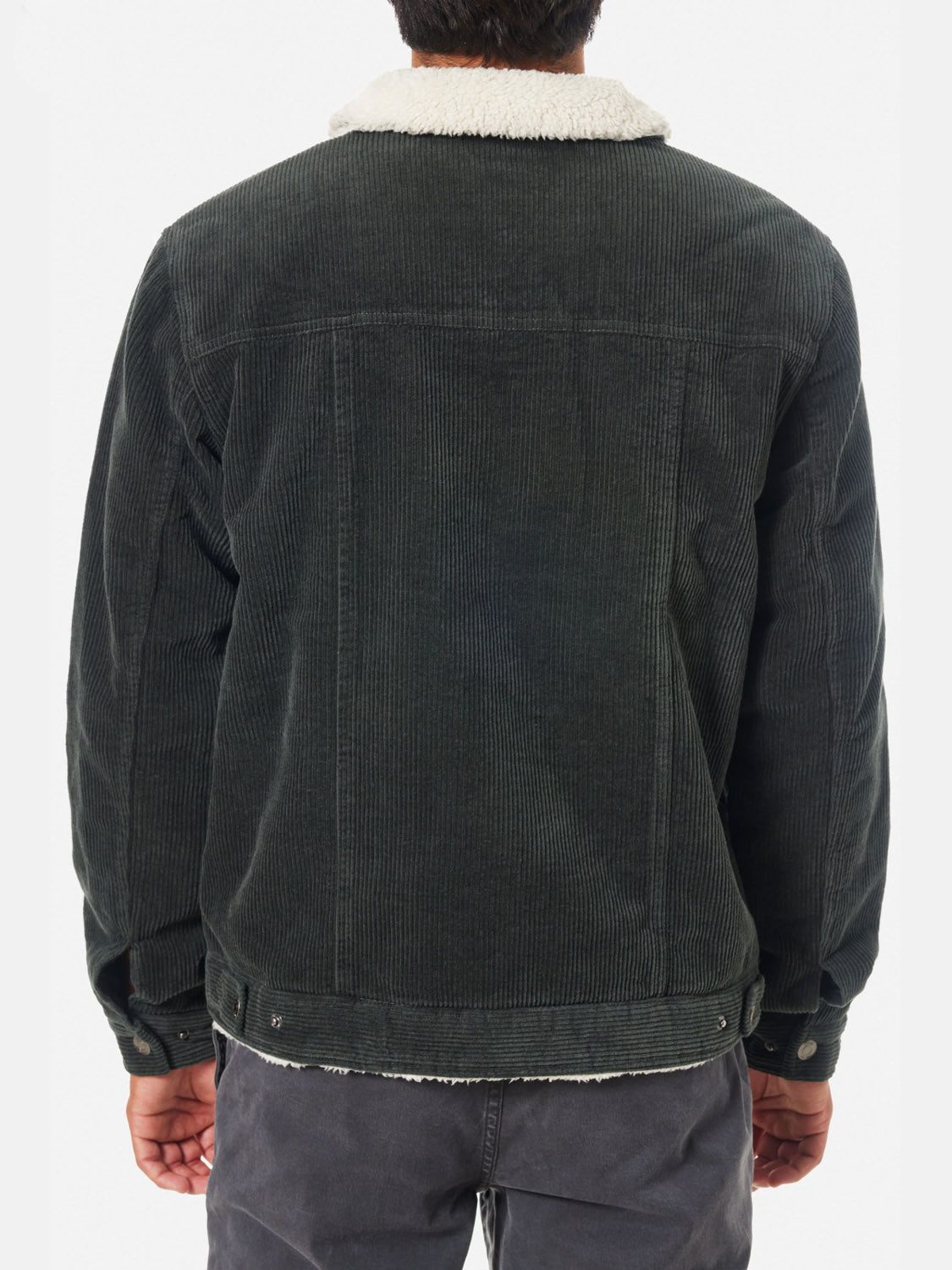 A person is seen from the back wearing the Katin Harris Corduroy Jacket in dark green, featuring a light sherpa-lined collar, visible seams, and buttoned cuffs, paired with dark gray pants.