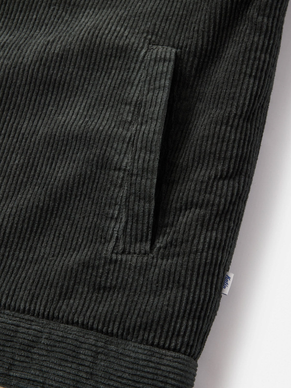 Close-up of the Katin Harris Corduroy Jacket in black, featuring a vertical front pocket, ribbed texture, and a small white tag with blue writing near the bottom right seam.