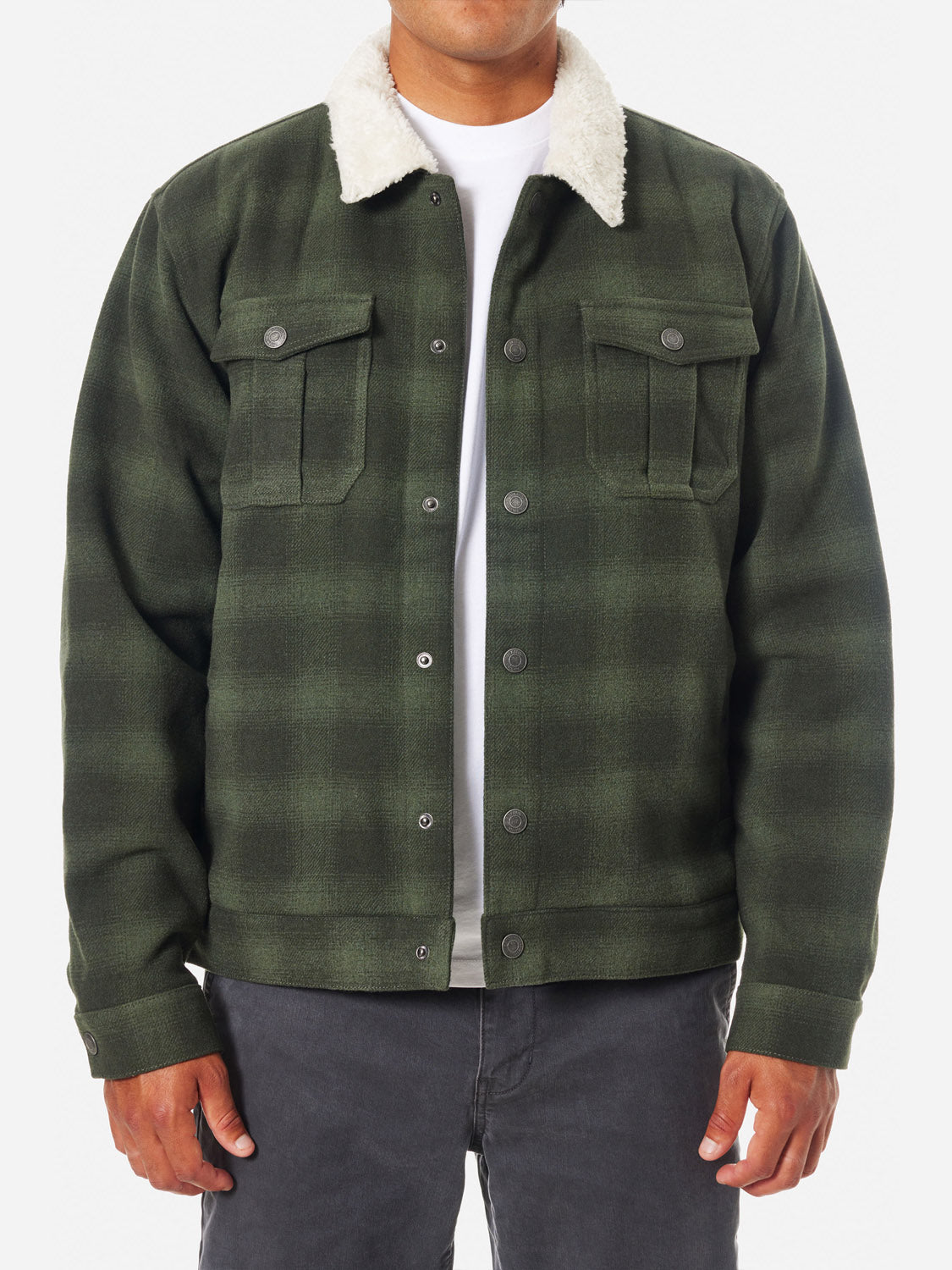Dressed against a plain white background, a person wears a Katin Harris Plaid Jacket with a white sherpa liner and green tones, buttoned down the front. Beneath is a white shirt, paired with dark pants.