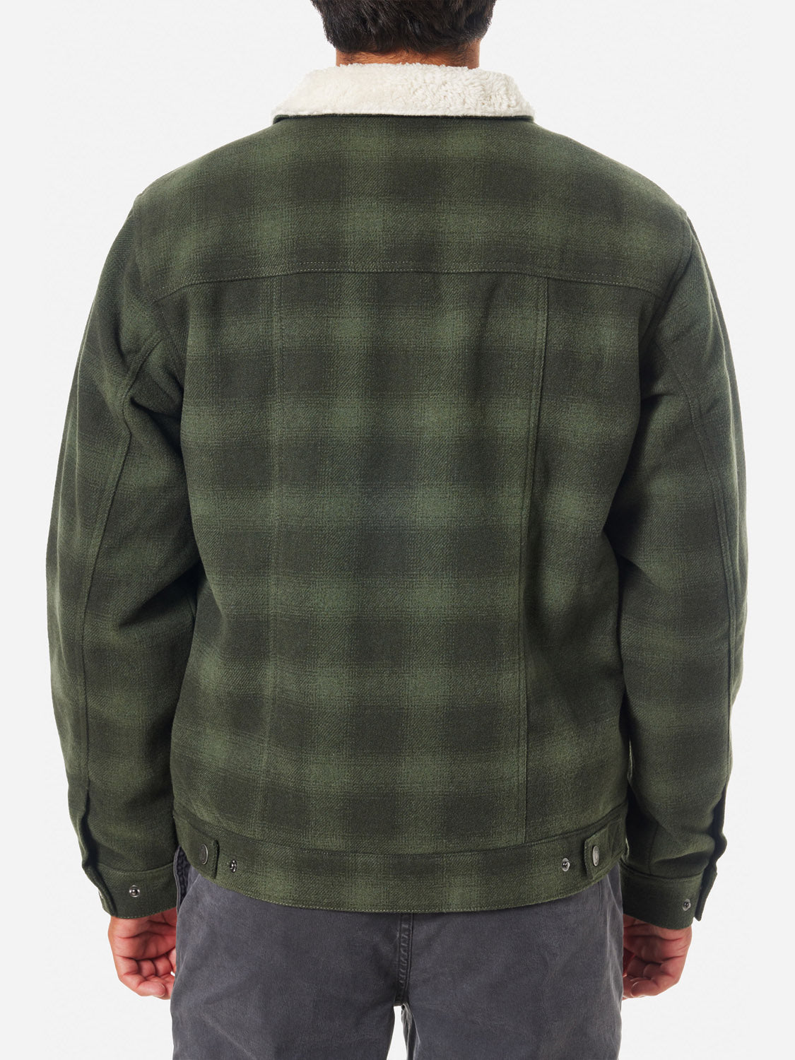 A person is seen from behind wearing a green Katin Harris Plaid Jacket with a white sherpa liner against a plain background. They are dressed in gray pants, and the jacket, from brand Katin, has button details at the bottom.