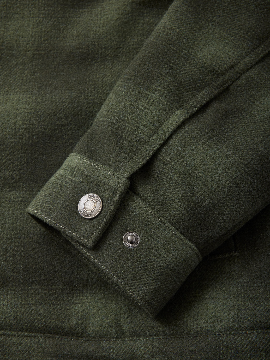 Close-up of a dark green plaid sleeve resembling the Katin Harris Plaid Jacket, with a buttoned cuff featuring silver snap buttons. The fabric is soft and textured, with visible edge stitching.