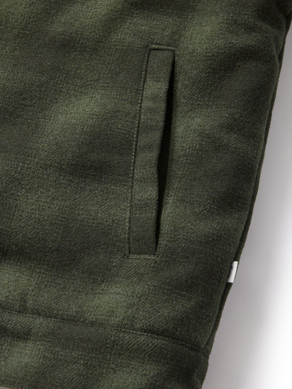 Close-up of a green textured Katin Harris Plaid Jacket, featuring a vertical slit pocket on the left. Neat stitching and a small white tag highlight quality craftsmanship. The fabric looks soft and cozy.