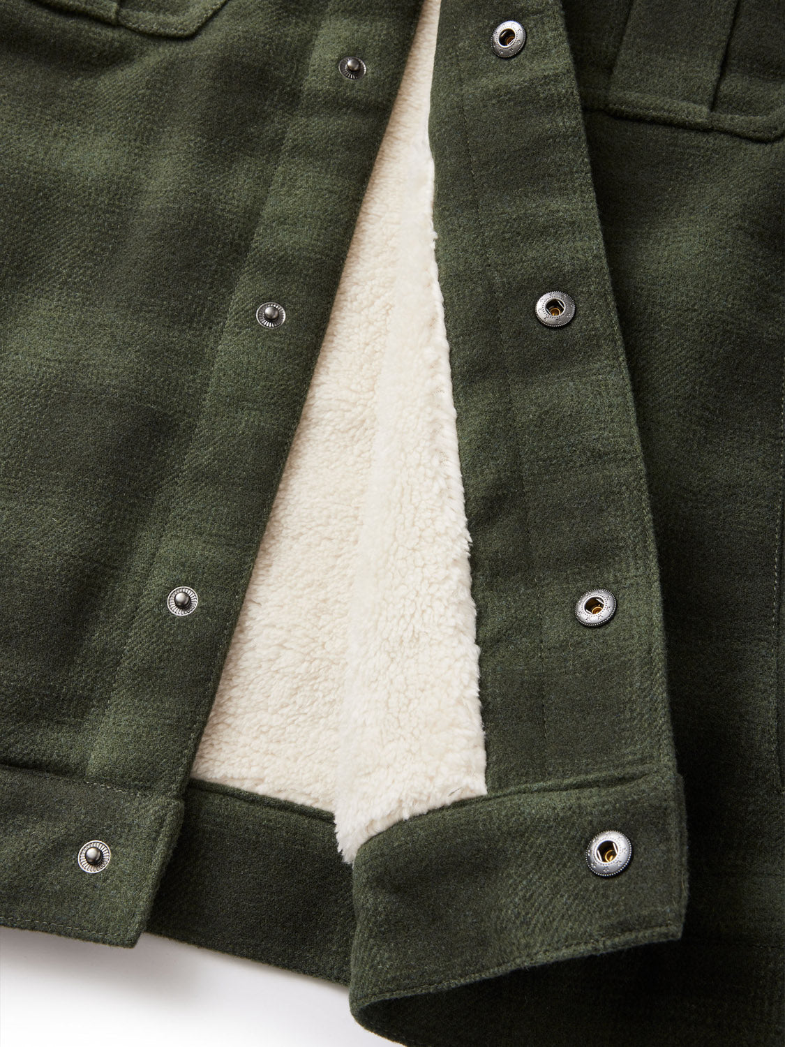 Close-up of an open dark green Katin Harris Plaid Jacket featuring silver snap buttons and a soft, white fleece lining. The textured fabric is well-stitched at the edges, offering a cozy contrast to this elegantly crafted garment by Katin.