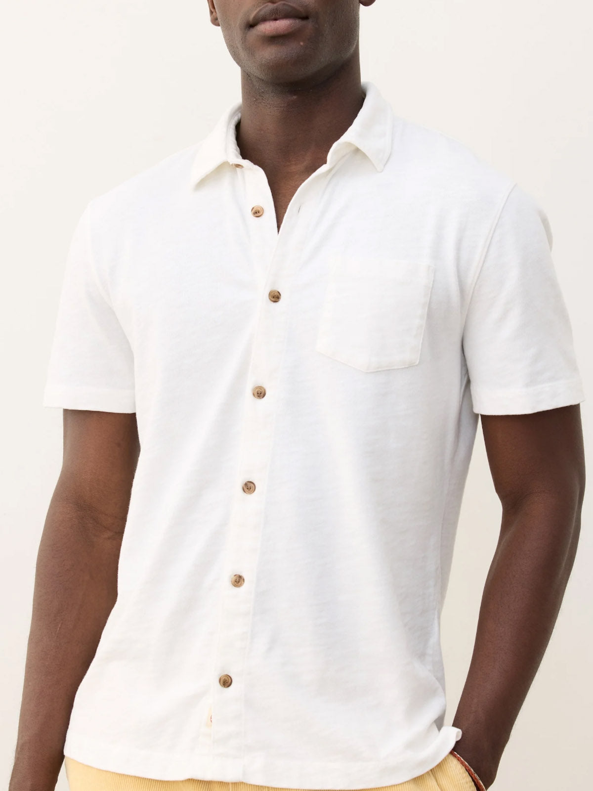 A man wears the Marine Layer Vintage Heavy Slub Button Down—a short-sleeve, 100% cotton, white shirt with a chest pocket and textured vintage slub—standing against a plain light background. Only his upper body is visible.