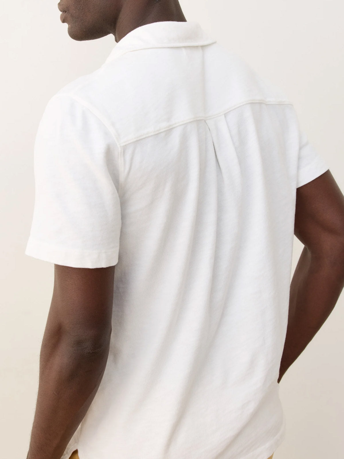 A person is shown from the back wearing the Marine Layer Vintage Heavy Slub Button Down, a white, short-sleeve collared shirt. The plain, neutral background highlights only their upper body.