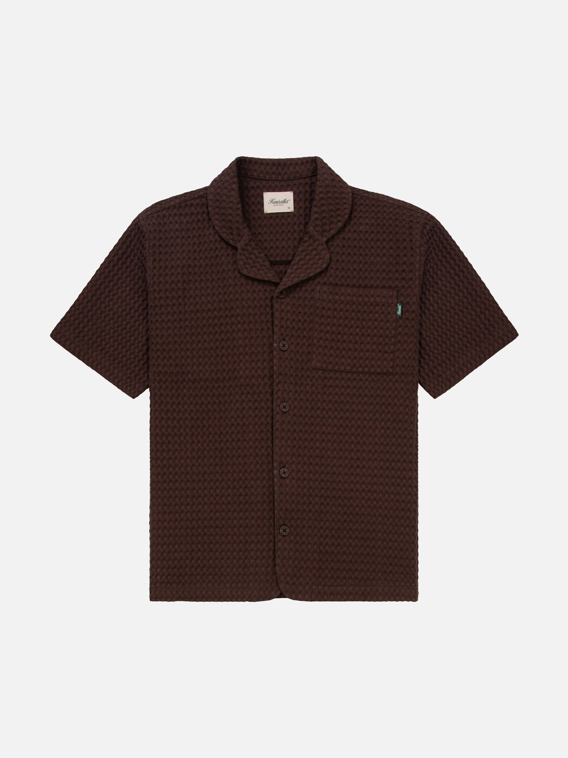 The Kuwalla Heavy Waffle Shirt by Kuwalla is a dark brown, cozy fabric short-sleeve with a waffle texture. It features a button-down front, single chest pocket with a green tag, relaxed fit, and notched collar, elegantly displayed on a white background.