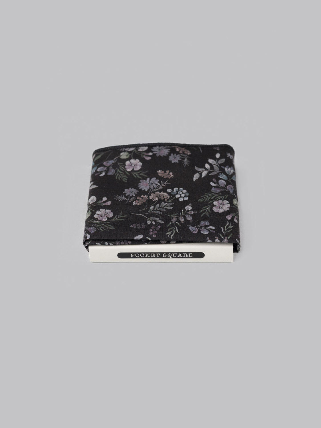 A folded black Liberty™ Hedgerow Pocket Square by ID Menswear, featuring a subtle purple and gray floral pattern on luxurious Tana Lawn cotton, displayed on a light gray background with a Pocket Square label.