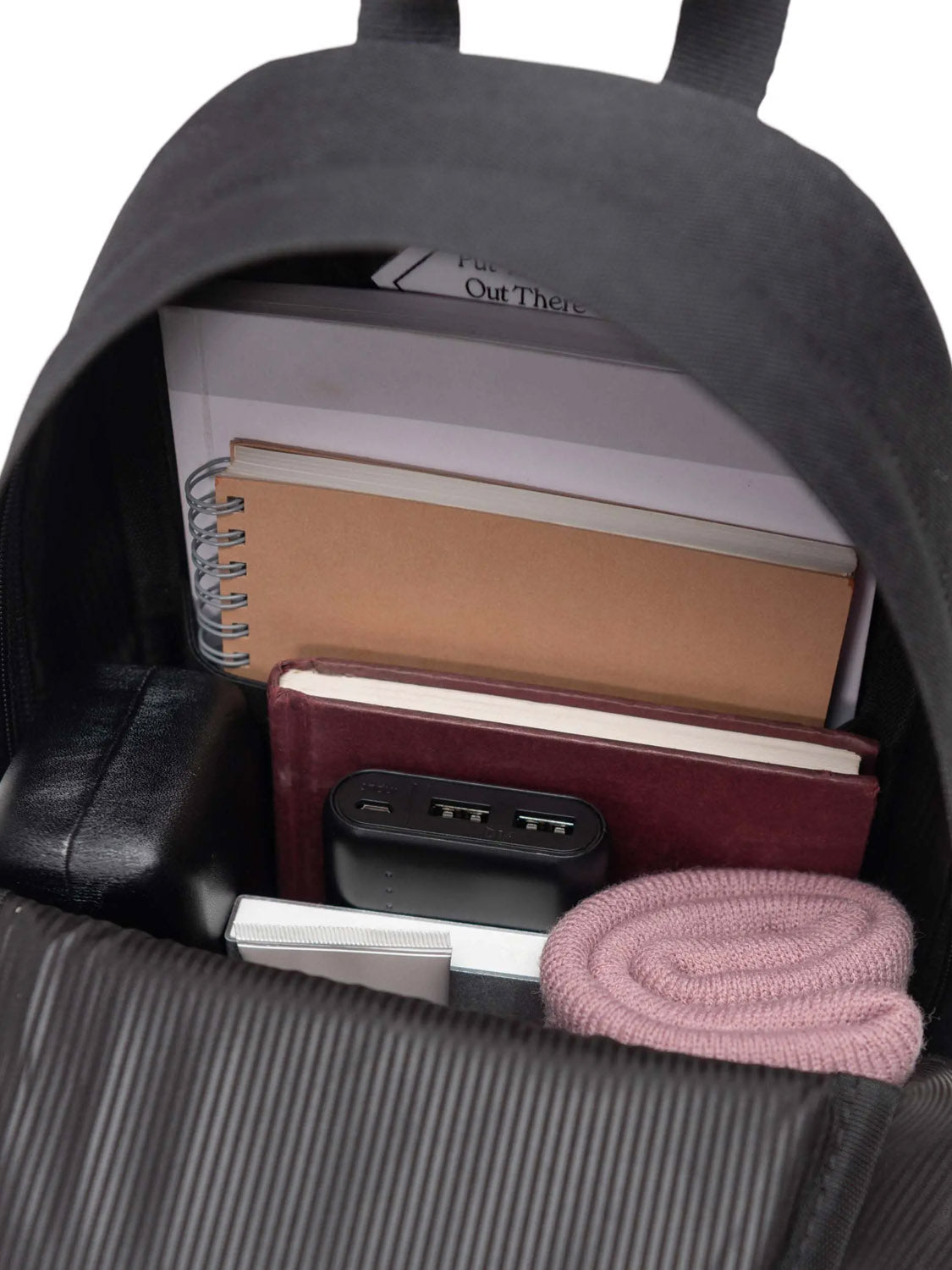 An open black Herschel Heritage Shoulder Bag - 8L, made from recycled polyester, holds notebooks, a spiral journal, a portable USB power bank, a black case, a folded pink scarf, and several documents.