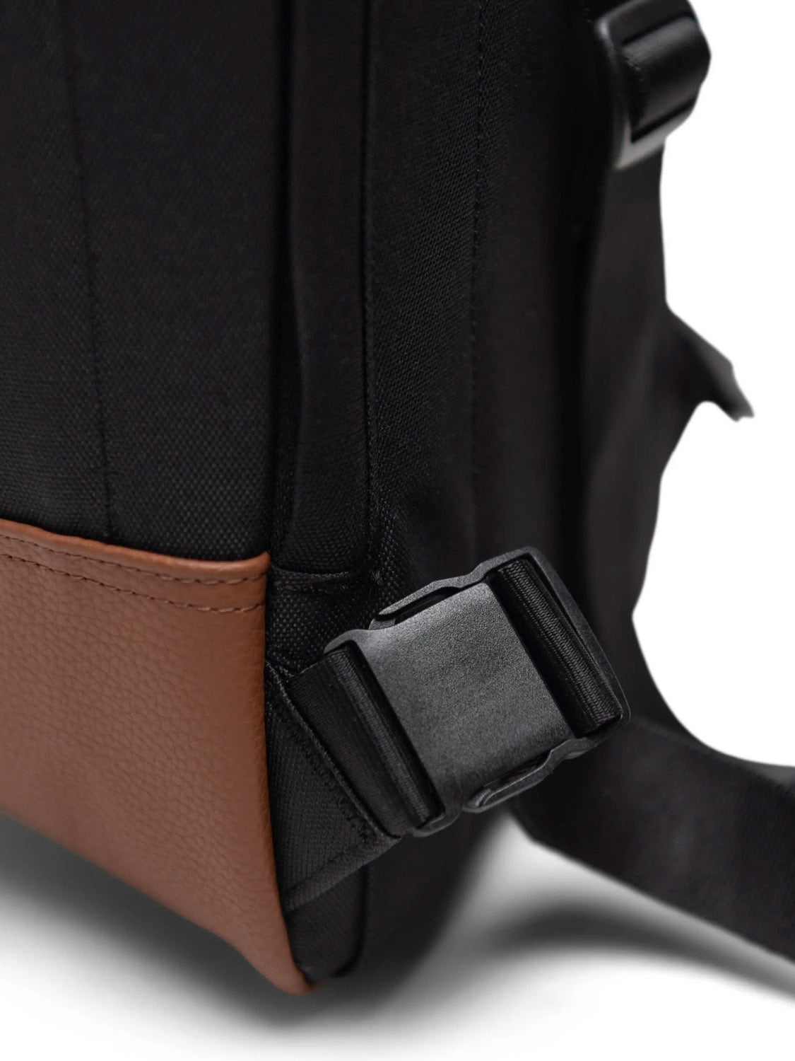 Close-up of the Herschel Heritage Shoulder Bag - 8L, featuring black and brown recycled polyester, a plastic buckle, adjustable strap on the side, and textured brown material at the bottom.