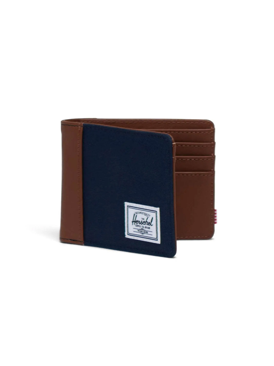 The Herschel Hank Wallet is a stylish bi-fold with brown leather sides, a navy blue fabric front, RFID blocking, multiple card slots inside, and a white rectangular Herschel logo patch for a secure and fashionable accessory.