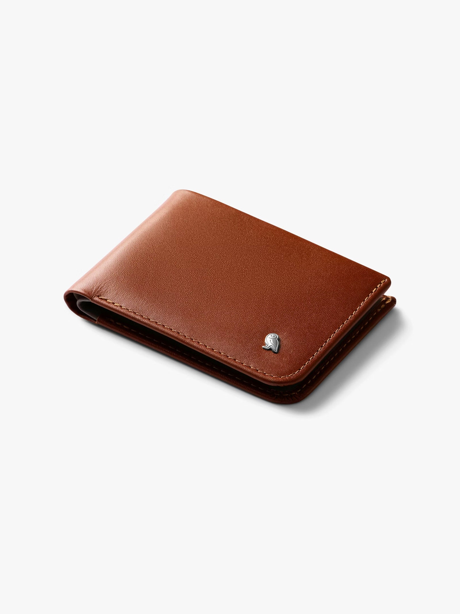 The Bellroy Hide and Seek Low Wallet, a brown eco-tanned leather bifold with RFID protection and a small silver emblem at the bottom right, is shown closed on a white background.