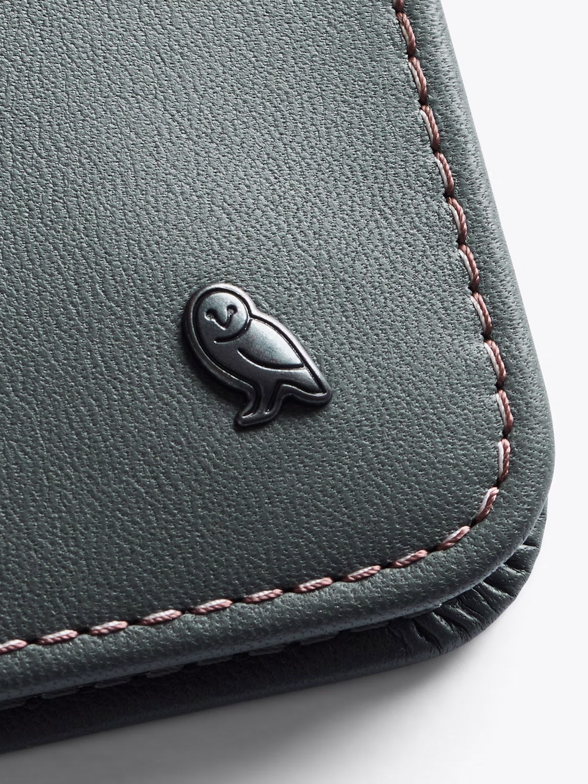 Close-up of the Bellroy Hide and Seek Low Wallet, crafted from dark eco-tanned leather with neat stitching and a small metal owl emblem in the corner.