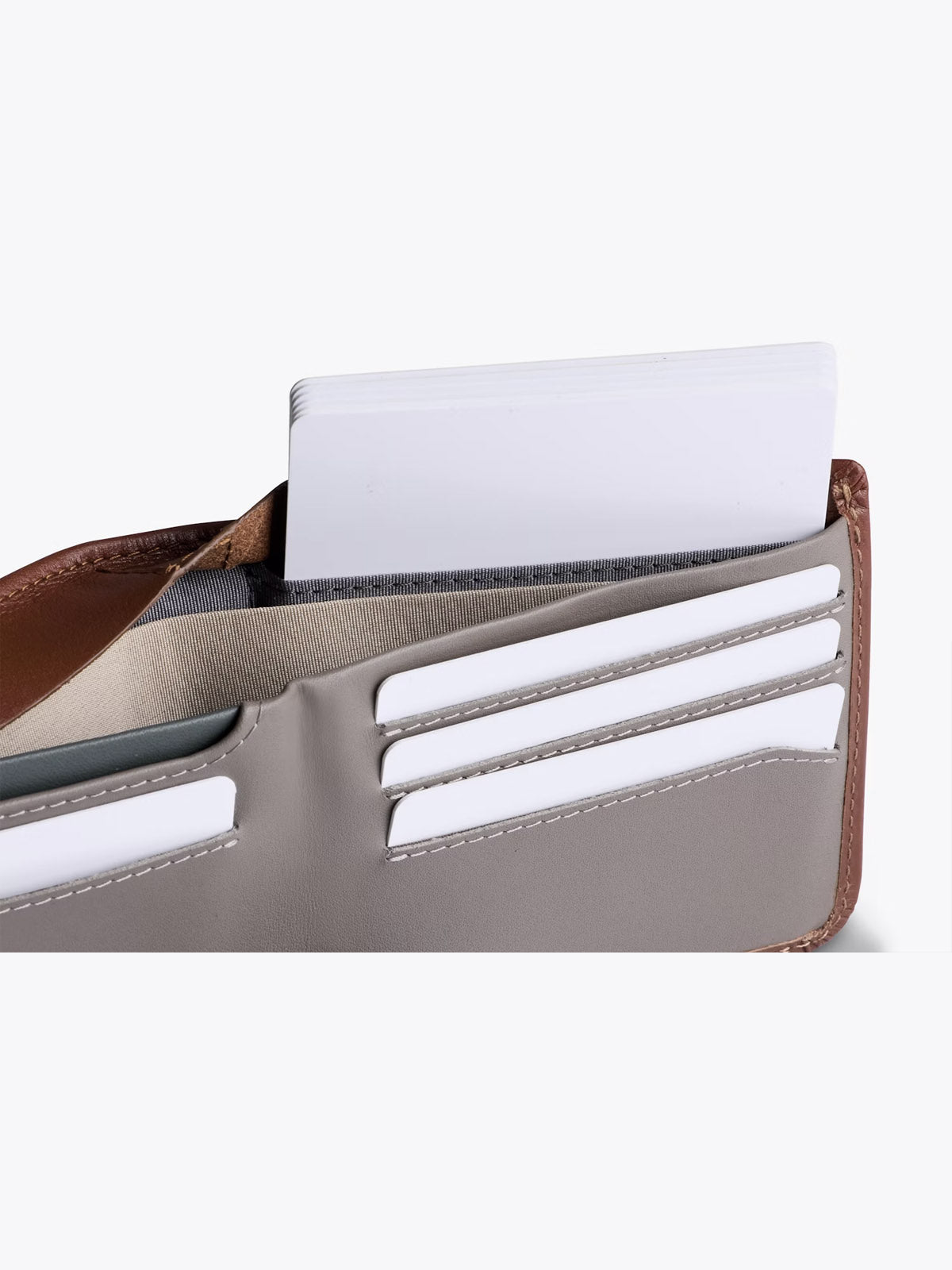 A close-up of the Bellroy Hide and Seek Low Wallet in brown and gray displays several white cards tucked into its slim leather card slots.