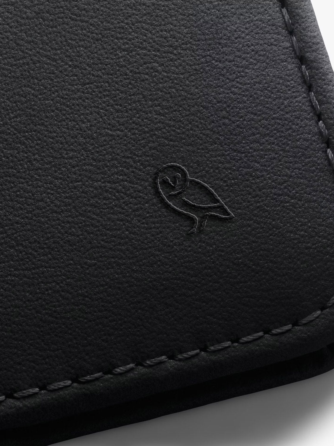 Close-up of black leather alternative with embossed owl logo and edge stitching, featured in the Bellroy Hide & Seek Innovera™ Edition wallet collection.