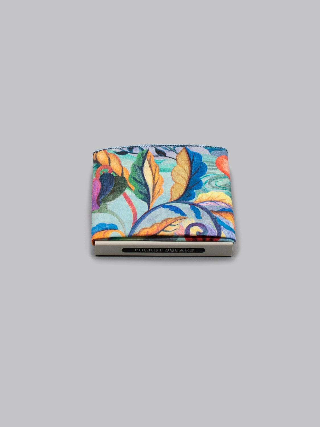 The ID Menswear Liberty™ Una Pocket Square, crafted from soft Tana Lawn cotton with a vibrant leaf and floral print, is neatly folded in a box labeled POCKET SQUARE against a plain gray background.