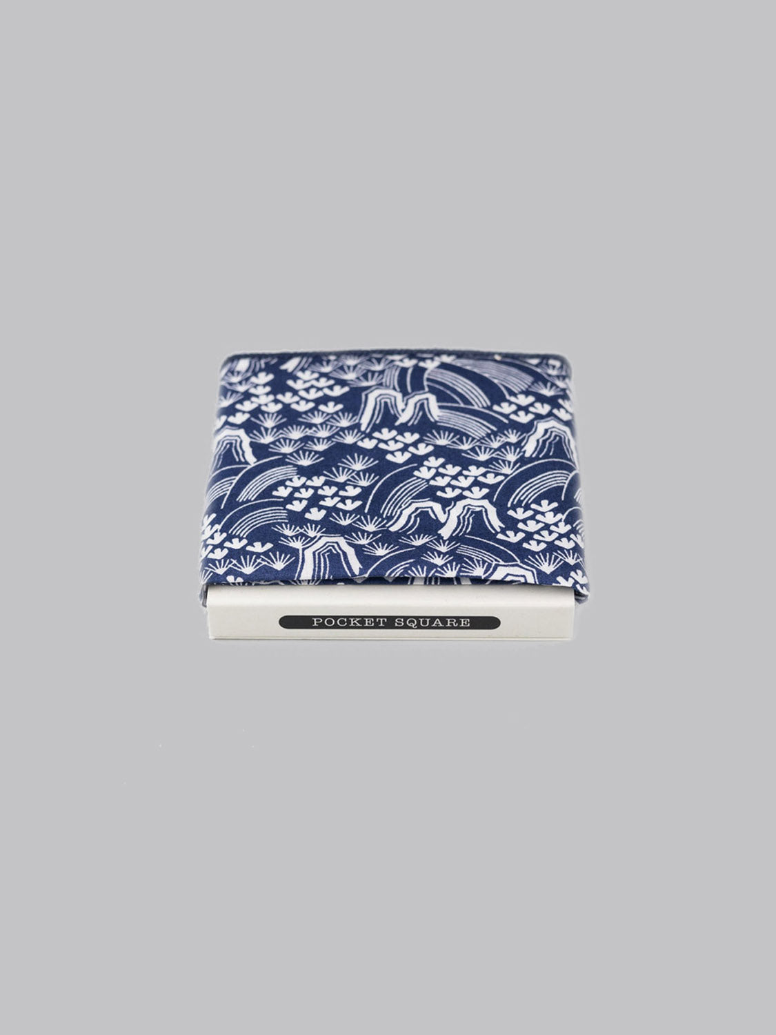A folded Liberty™ Hillside Pocket Square by ID Menswear, in blue and white Tana Lawn cotton, handmade in Brooklyn, rests atop a small white POCKET SQUARE box on a plain gray background.