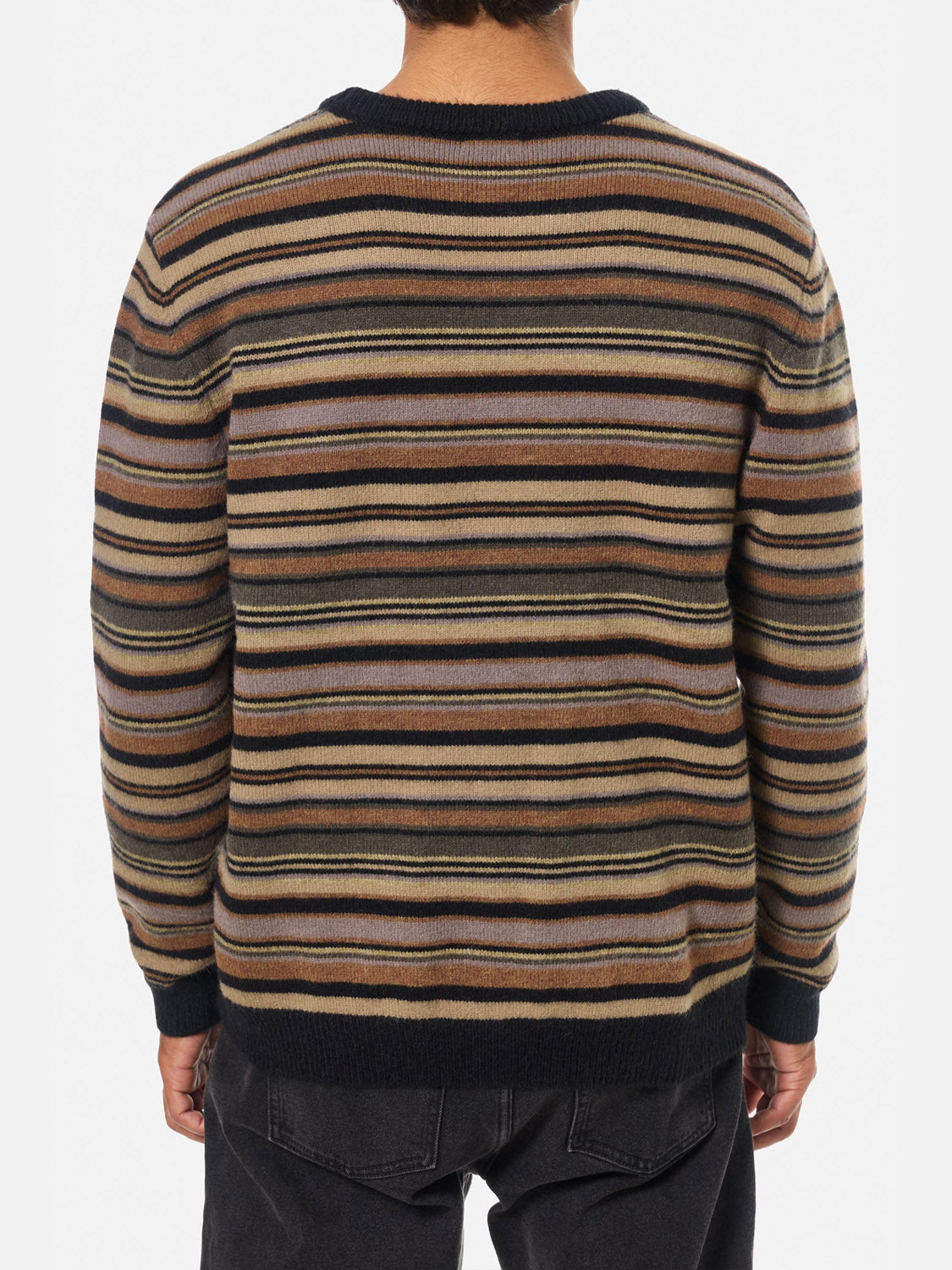 A person faces away from the camera, wearing Katin’s Hitch Sweater—a relaxed-fit piece made from ultra-soft blended yarn in a custom brown, beige, black, and gray stripe—paired with black pants.