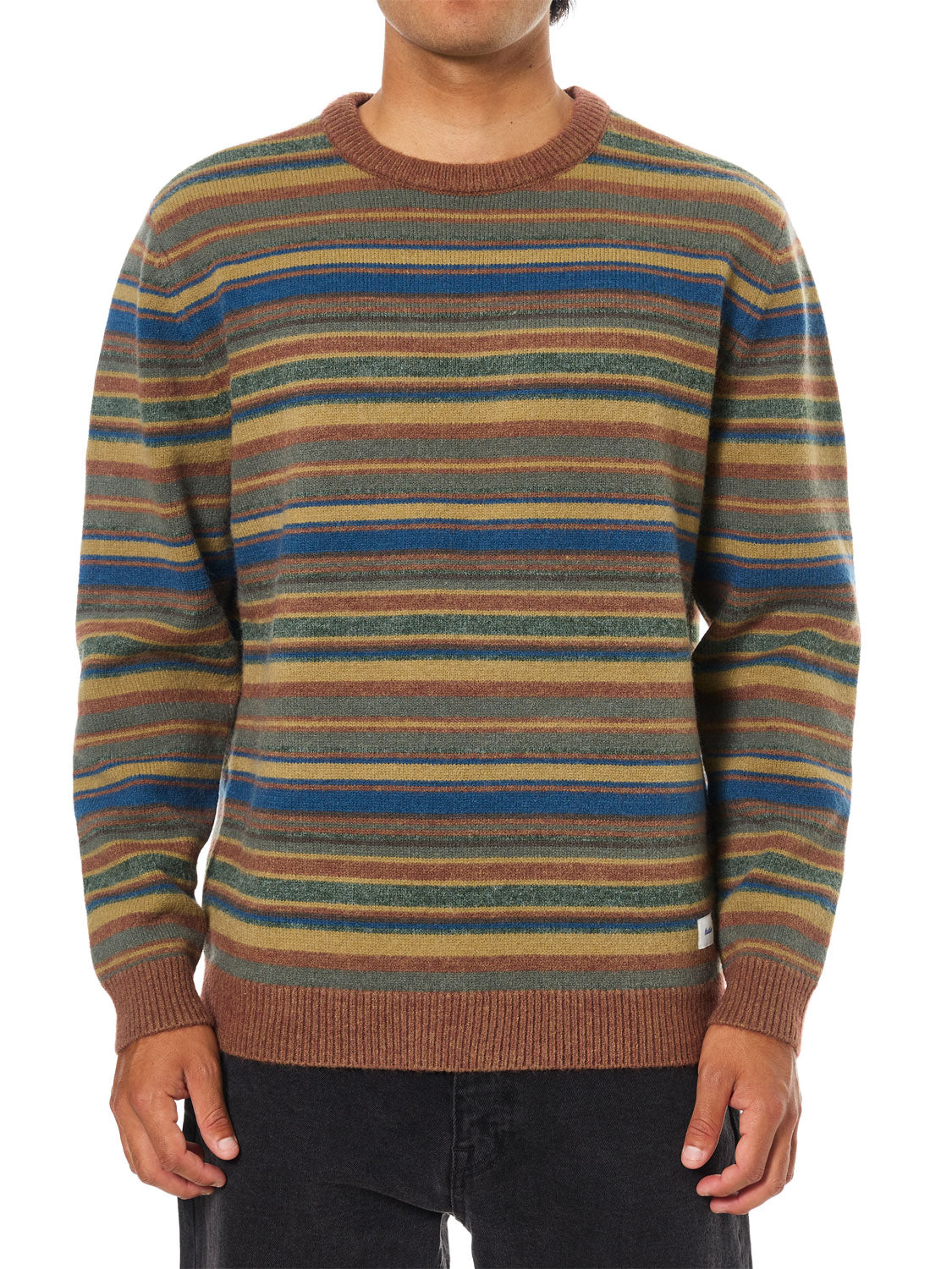 A person wears the Katin Hitch Sweater, featuring a custom brown, green, blue, and gray stripe pattern in ultra-soft blended yarn, paired with black pants. The background is plain white.