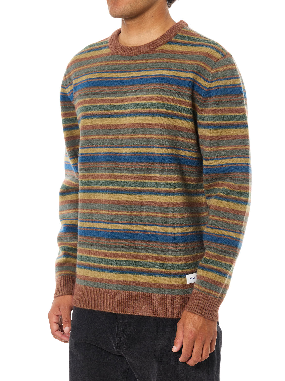 Wearing the Katin Hitch Sweater, which showcases a custom stripe pattern in brown, green, blue, and tan with ultra-soft blended yarn, paired with black pants and set against a white backdrop.