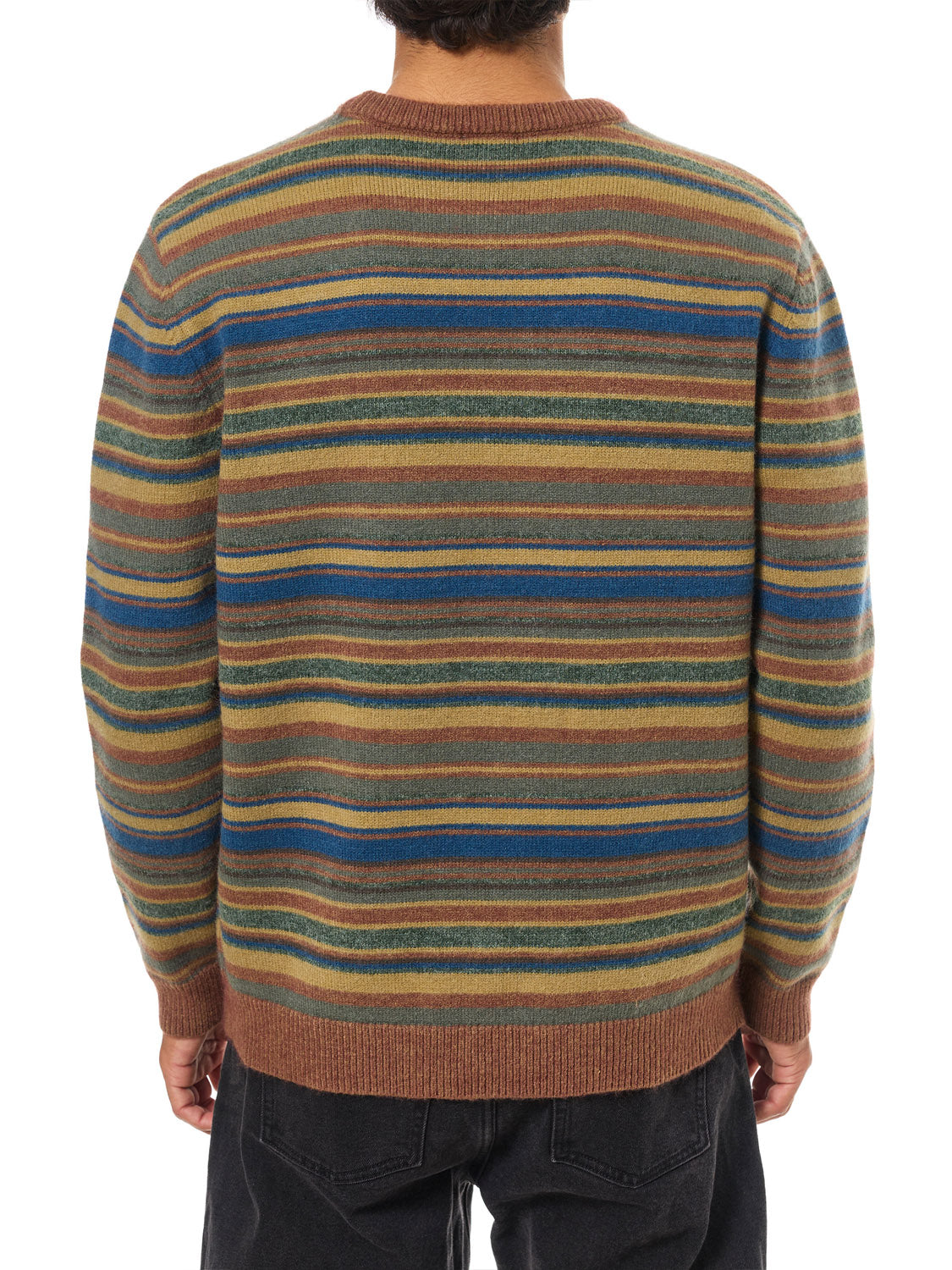 A person is seen from the back wearing the Katin Hitch Sweater, which has a custom stripe pattern in brown, green, blue, and tan, made from ultra-soft blended yarn, paired with dark pants.