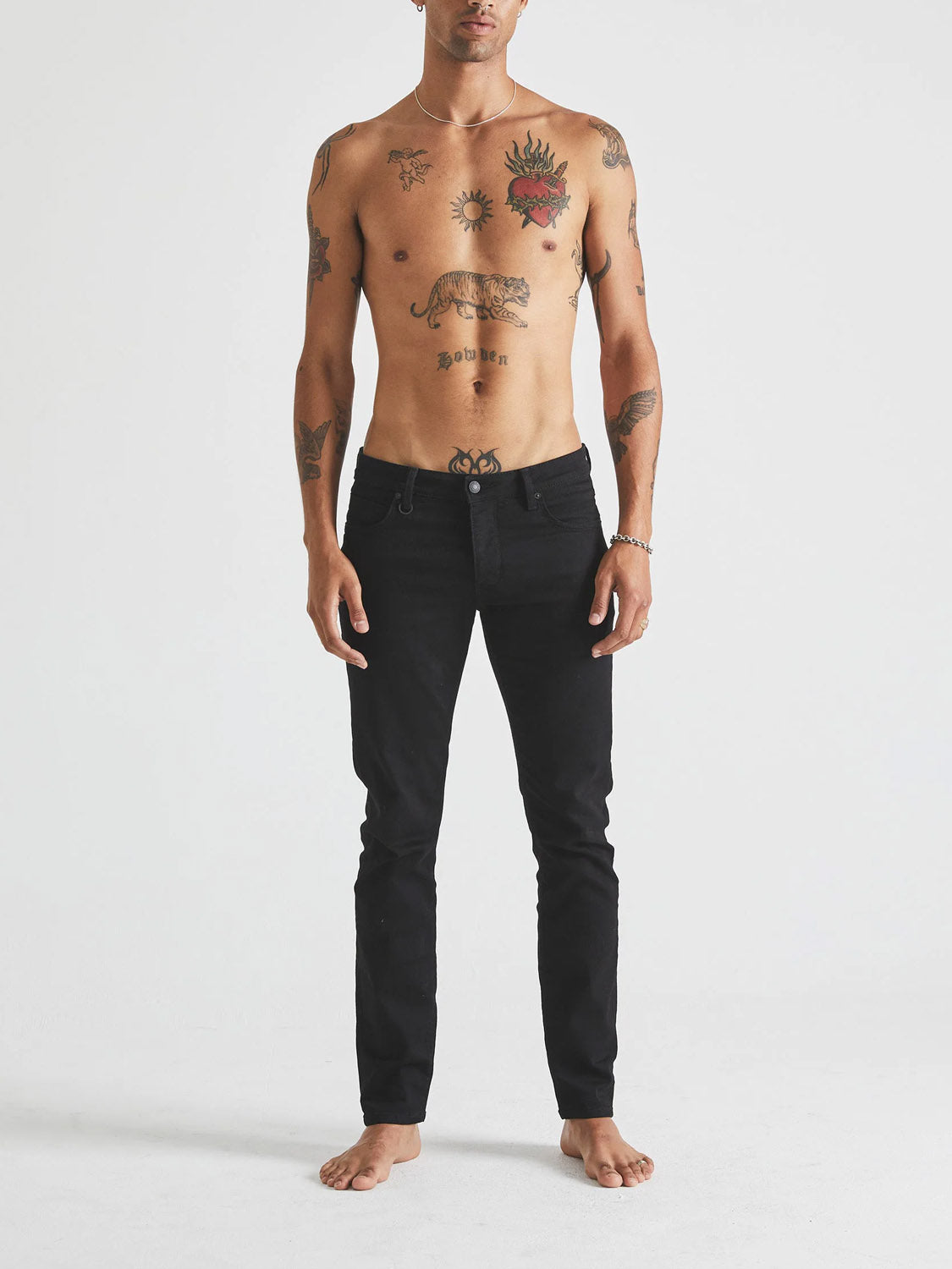 A barefoot, shirtless person with chest and arm tattoos faces forward wearing Neuw's Iggy Skinny Perfecto black jeans against a plain white background.