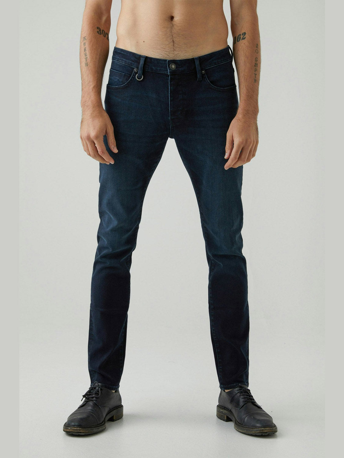 A shirtless person wearing Neuw's Iggy Skinny Polar jeans and black shoes stands against a light background, arms relaxed by their sides. Only their body from the shoulders down is visible.