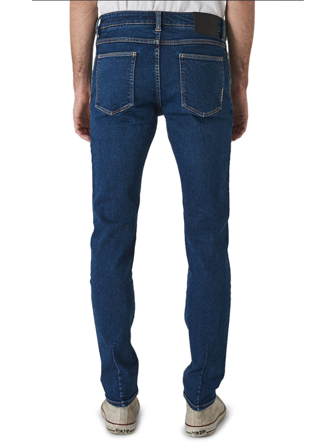 A man is shown from the back against a white background, wearing Neuw's Iggy Skinny Zero Utility Blue jeans with a slim waist, visible stitching on the back pockets, and white sneakers.