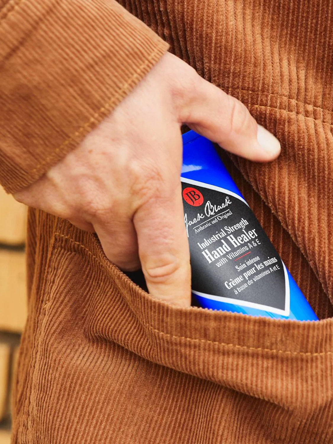 A hand slips a blue tube of Jack Black Industrial Strength Hand Healer 3oz—ideal for dry hands—into the pocket of light brown corduroy pants.