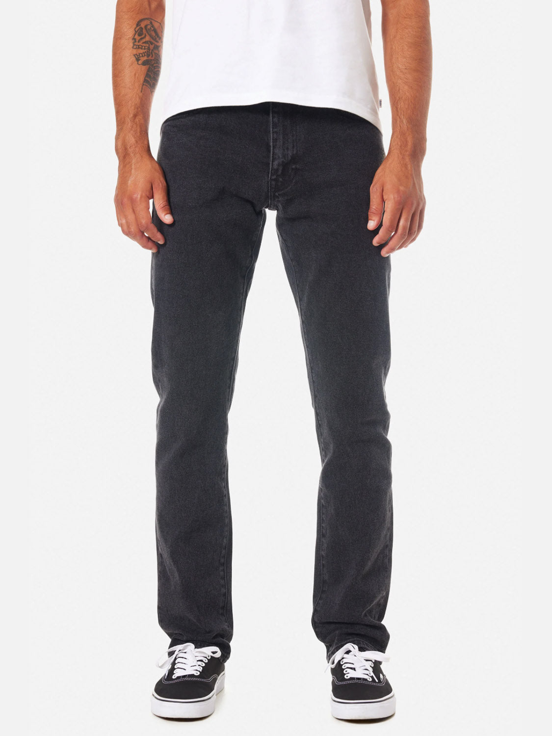 A person wears Katin’s Jacob 71 Slim Straight Pants in mid-rise, classic 5-pocket style with a white tee and black-and-white sneakers. Their tattooed left arm is visible. The image, cropped at the shoulders, shows them standing against a white background.