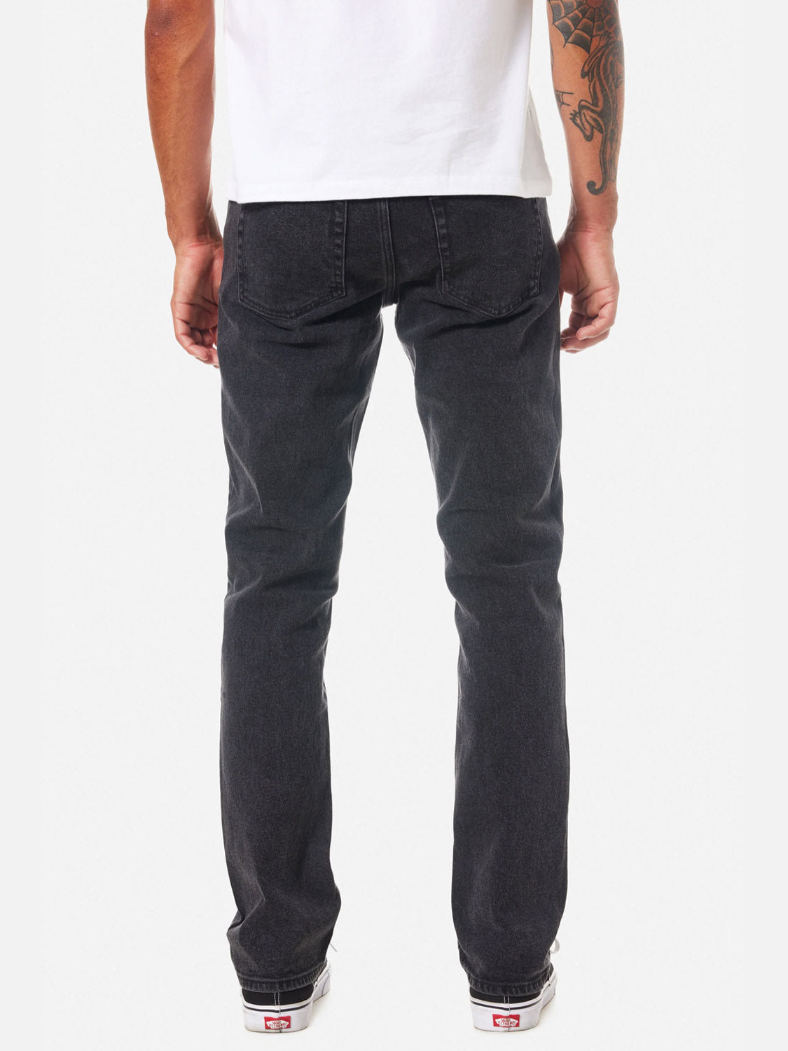 A person wearing a white t-shirt, Katin Jacob 71 Slim Straight Pants, and white sneakers is shown from the back with a visible arm tattoo. The background is plain and light-colored.