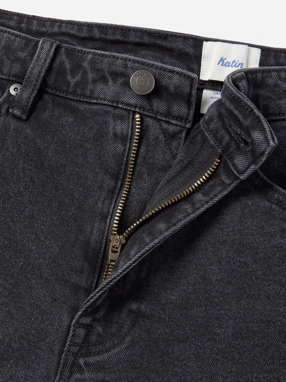 Close-up of Katin Jacob 71 Slim Straight Pants in dark gray denim, featuring a mid-rise, open brass zipper and button fly, waistband with brand label detail, and classic 5-pocket design.