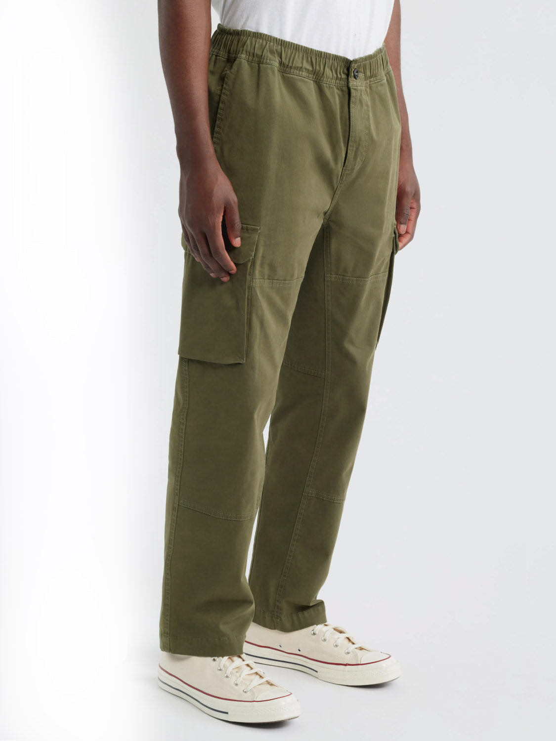 Someone wearing Rails Jaiden Cargo Pants in olive green, paired with a white t-shirt and white low-top sneakers, stands against a plain white background.