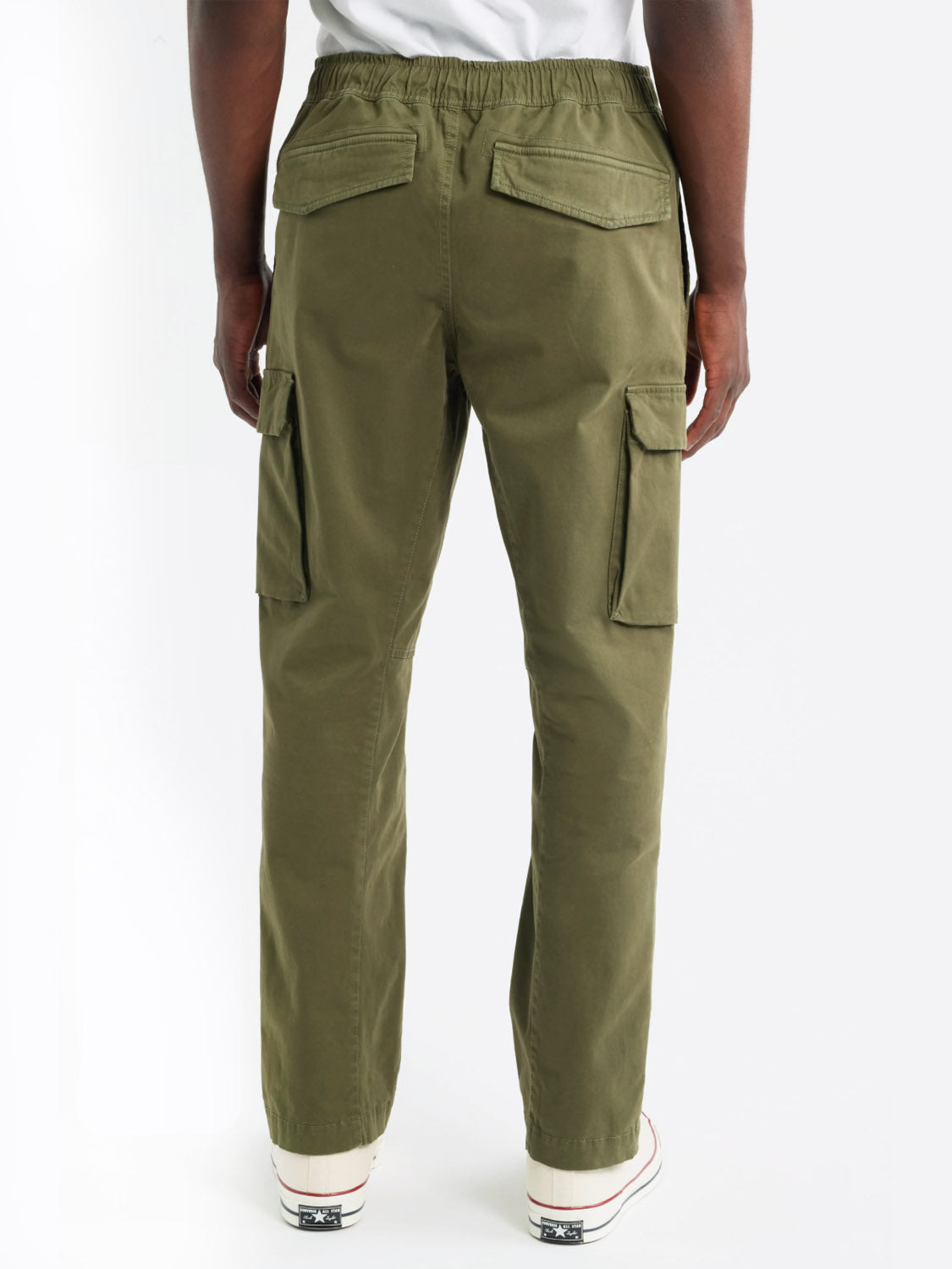 A person is shown from the back in a plain, light setting, wearing olive green Jaiden Cargo Pants by Rails with flap pockets and white sneakers featuring black details.
