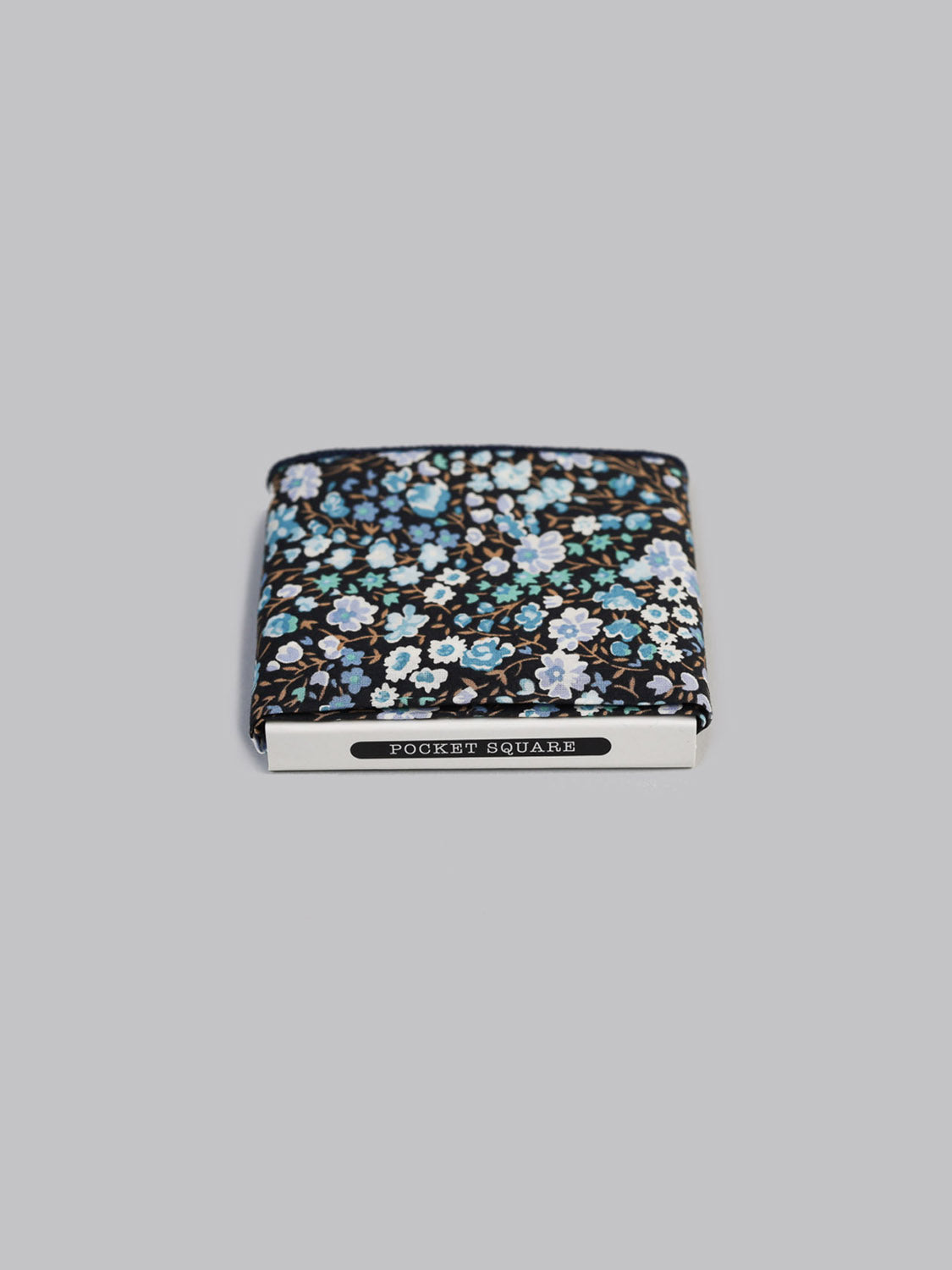 A Liberty™ Jo Pocket Square by ID Menswear in blue, white, and green floral Tana Lawn cotton is neatly folded in a box labeled POCKET SQUARE, set against a plain gray background.