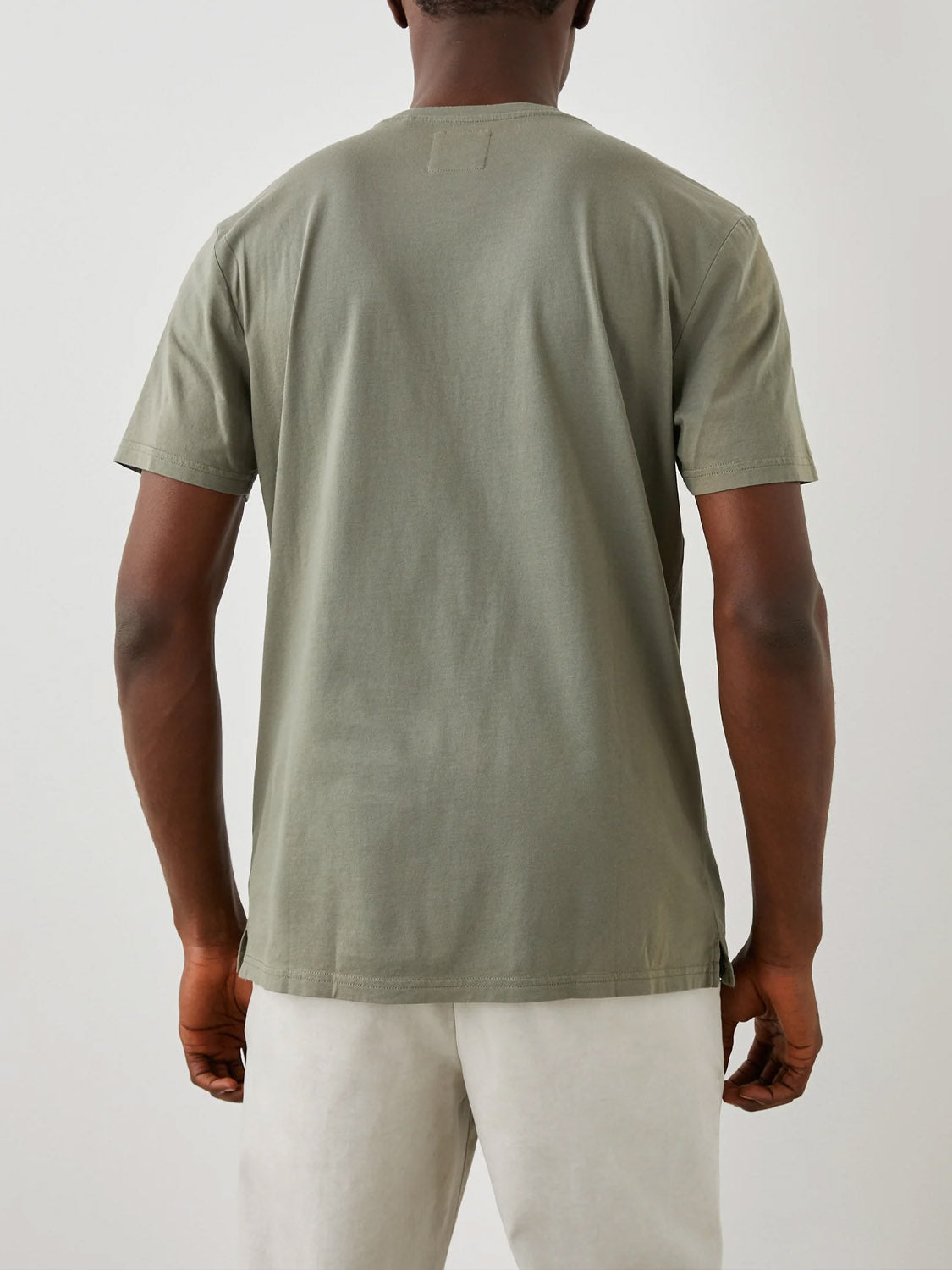 A person in a Rails Johnny Tee, featuring a plain olive green vintage wash and classic fit, stands with their back to the camera, paired with light-colored pants against a simple light gray background.