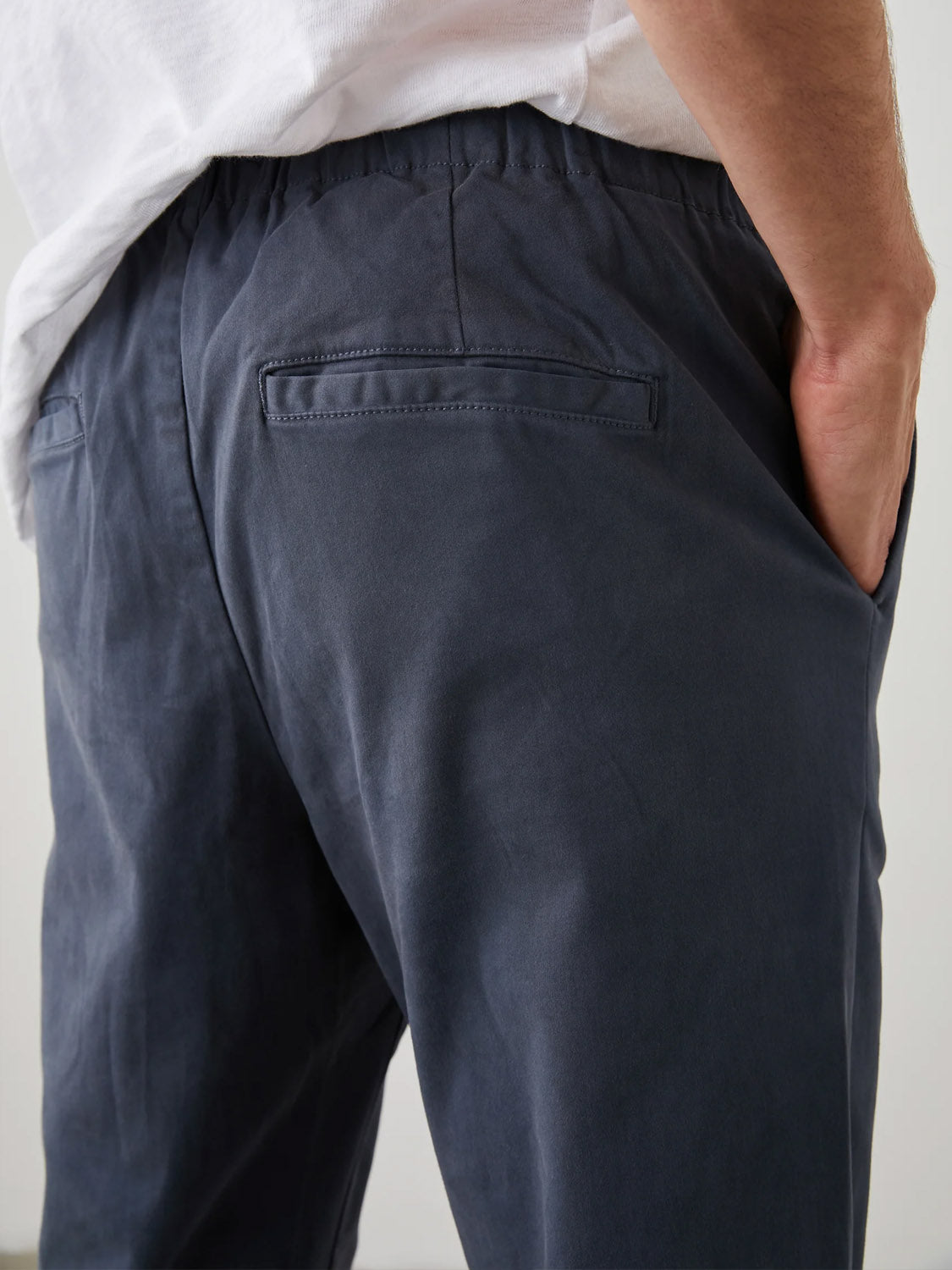 A person wearing the Rails Julian Pant in dark navy-blue stretch twill, hands in pockets. These pants offer a comfortable fit with subtle stitching and pair effortlessly with a white shirt for a classic yet relaxed vintage look.