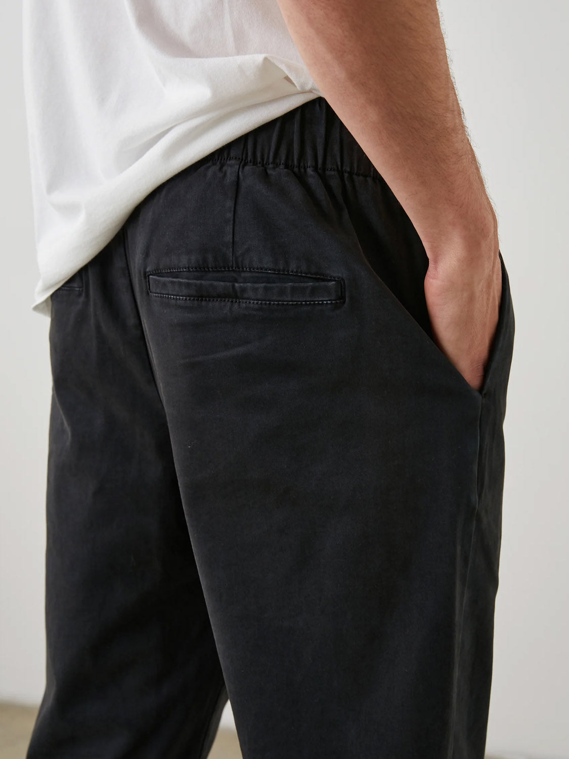 A person wearing a white t-shirt and the Rails Julian Pant with vintage vibes stands with one hand in their pocket. The pants, by Rails, feature an elastic waistband and a back pocket with a subtle black design, showcasing each detail.