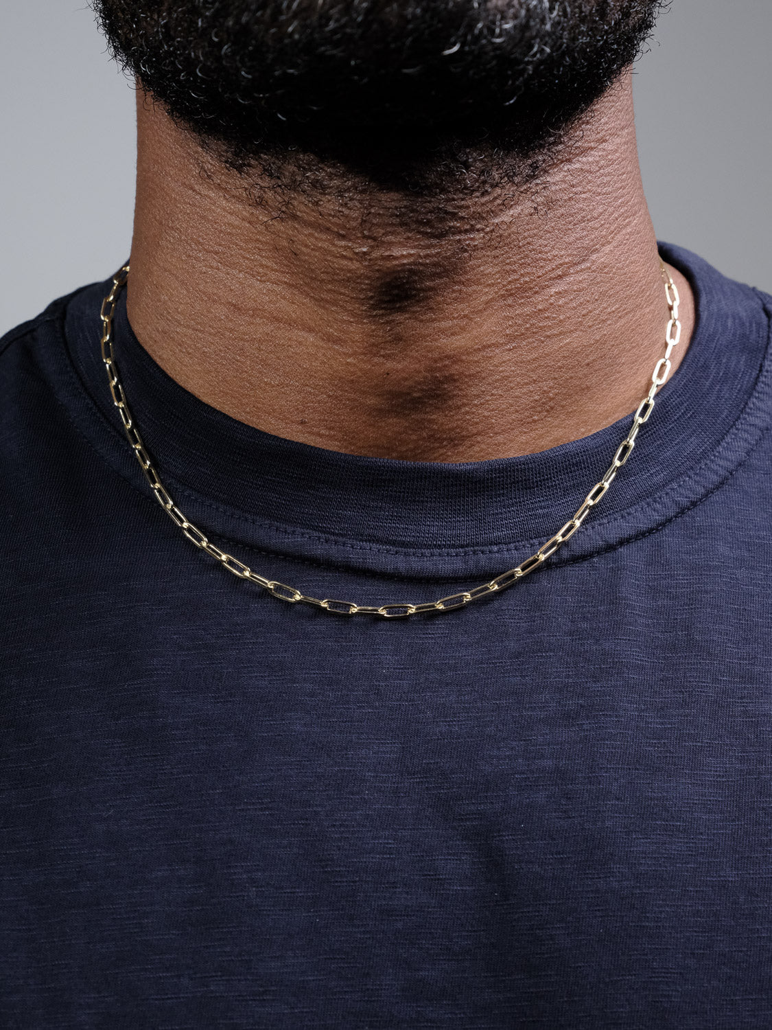 Close-up of a person wearing the Kai 100 Paper Clip Chain Necklace by ID Menswear, styled with a dark navy blue t-shirt. The lower face and neck are visible, showcasing the elegant chain—crafted in Italy.